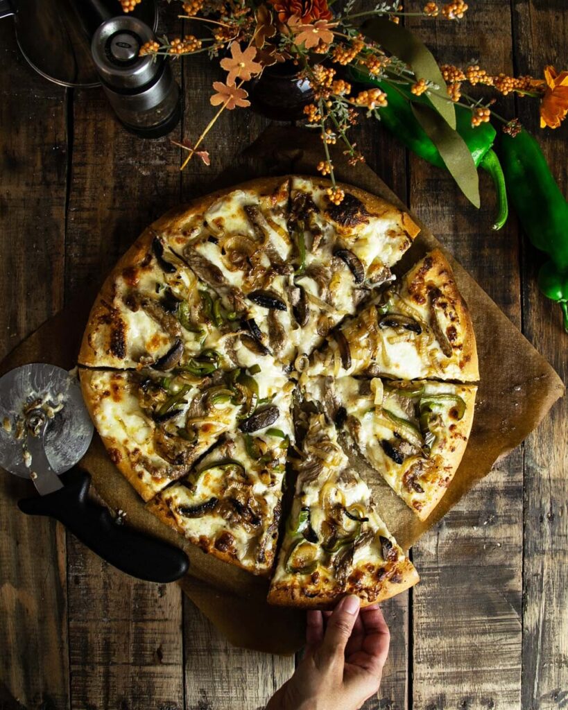 Top view of a Philly cheesesteak pizza, sliced and ready to eat