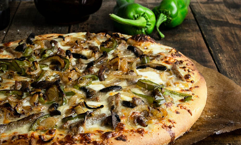 Philly cheesesteak pizza on a dark wood background
