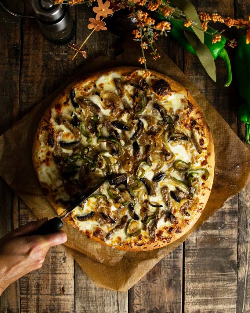 Slicing a Philly cheesesteak pizza with a pizza cutter, top view