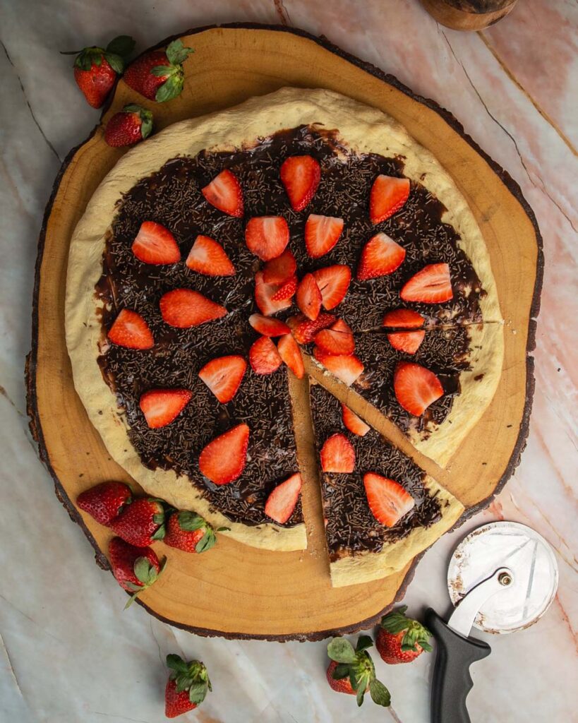 Brazilian sweet pizza with a slice cut out, on a tree truck cutting board.