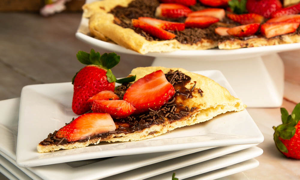 A slice of Brazilian pizza on a stack of white plates, with a handful of strawberries in front.