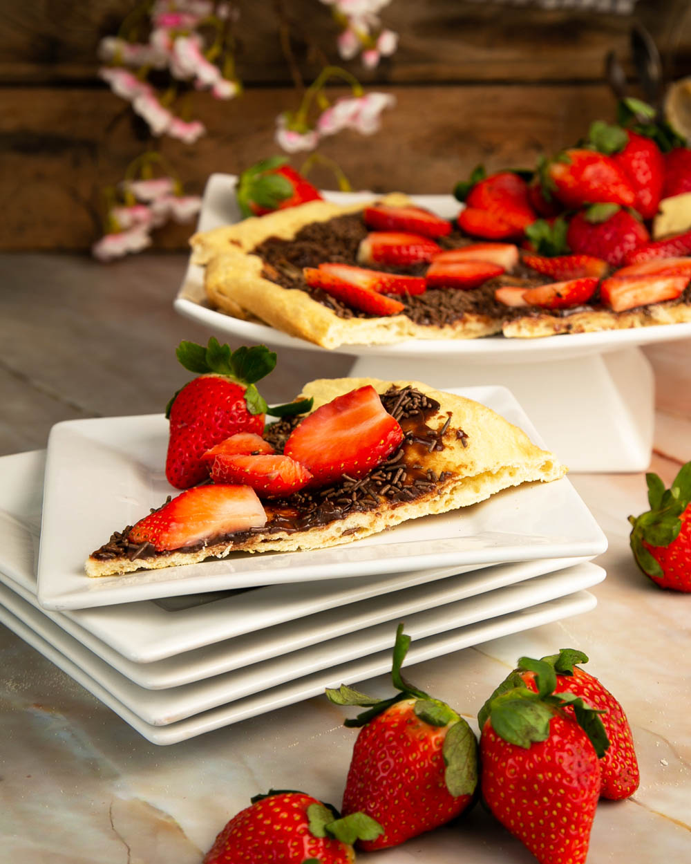 A slice of Brazilian pizza on a stack of white plates, with a handful of strawberries in front.
