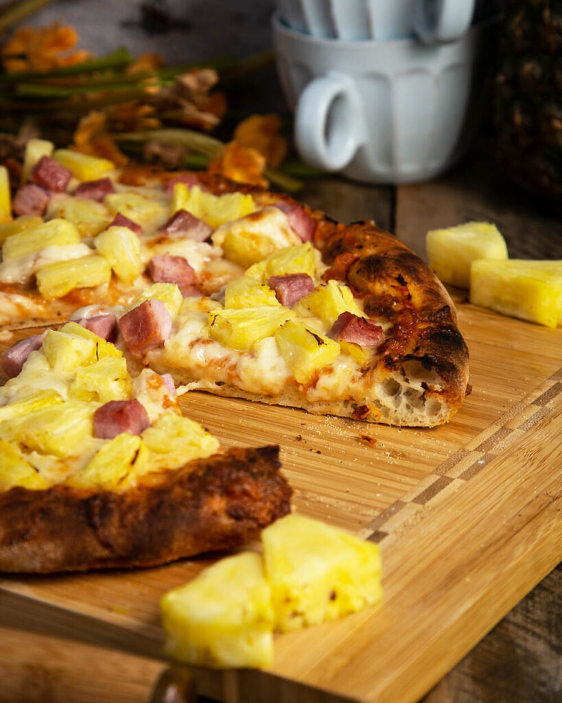 Side view of sliced Hawaiian pizza with ham and pineapples.