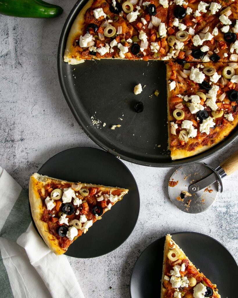 Slices of Greek style pizza on black plates with a marble background.
