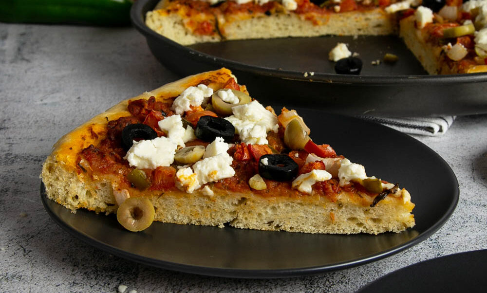 Side view of sliced Greek focaccia pizza topped with lots of olives and feta.