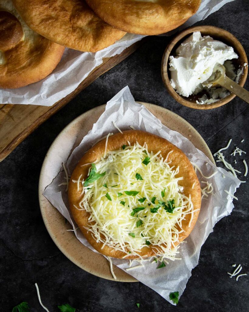 Hungarian Langos topped with sour cream and cheese, on a plate and marble countertop.