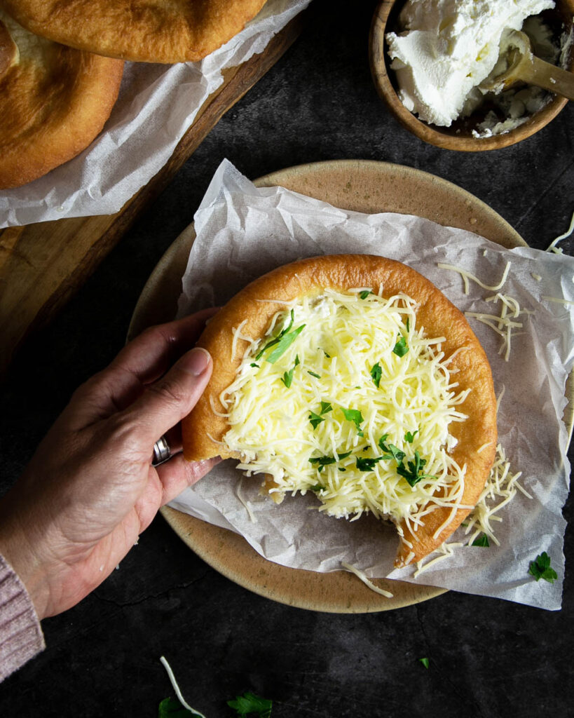 holding a half eaten Langos topped with the sour cream and cheese with a marble background.