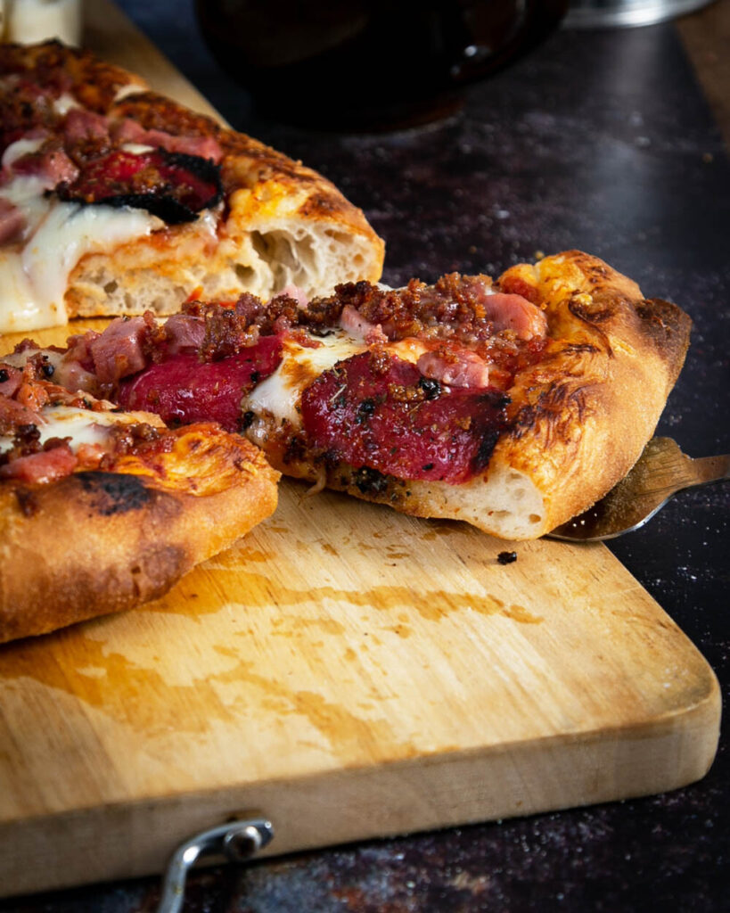 Taking a slice of meat lovers pizza on a wood cutting board.