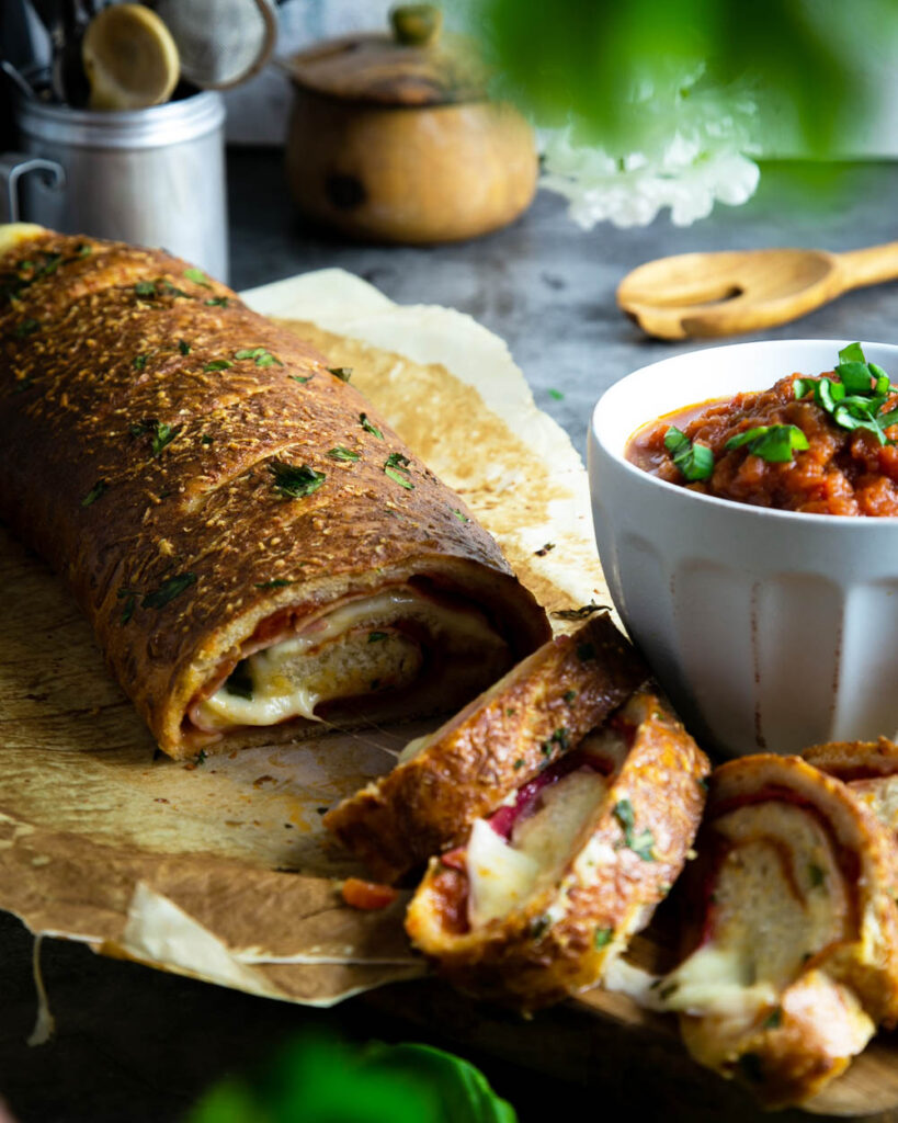 A Philadelphia Stromboli stuffed with ham and salami on parchment, with a side of marinara.