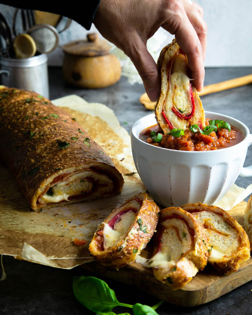 Dipping a slice of deli Stromboli in marinara sauce, on a cutting board with parchment.