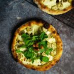 Top view of pizza bianca on a marbled surface topped with fresh arugula and garlic