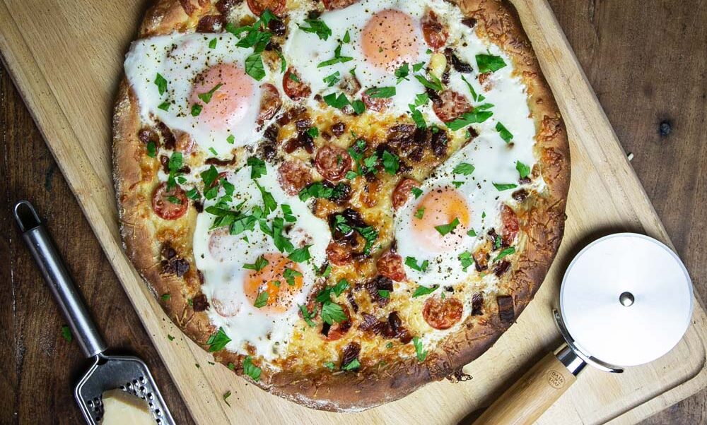 Top view of the classic breakfast pizza with sunny side up eggs on a wooden cutting board.