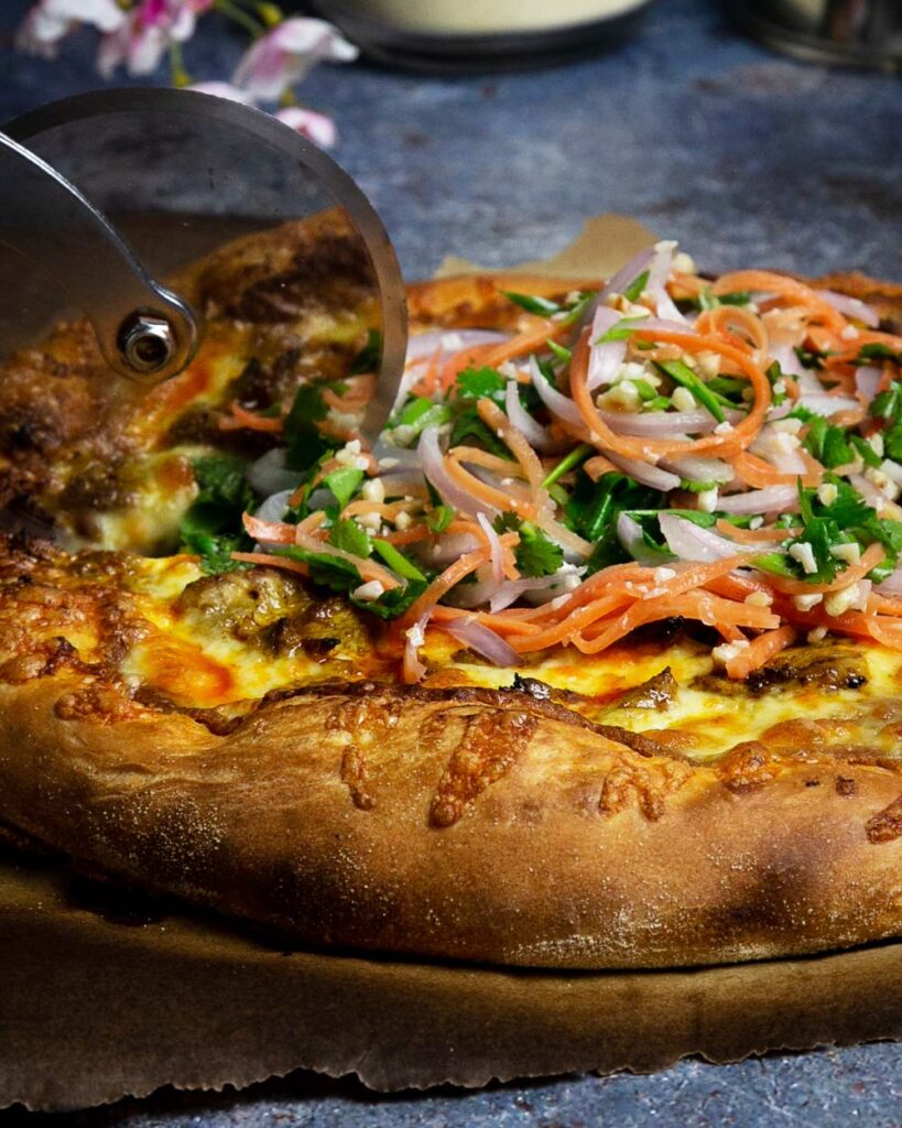 Side view, slicing the Thai satay pizza with a pizza wheel.