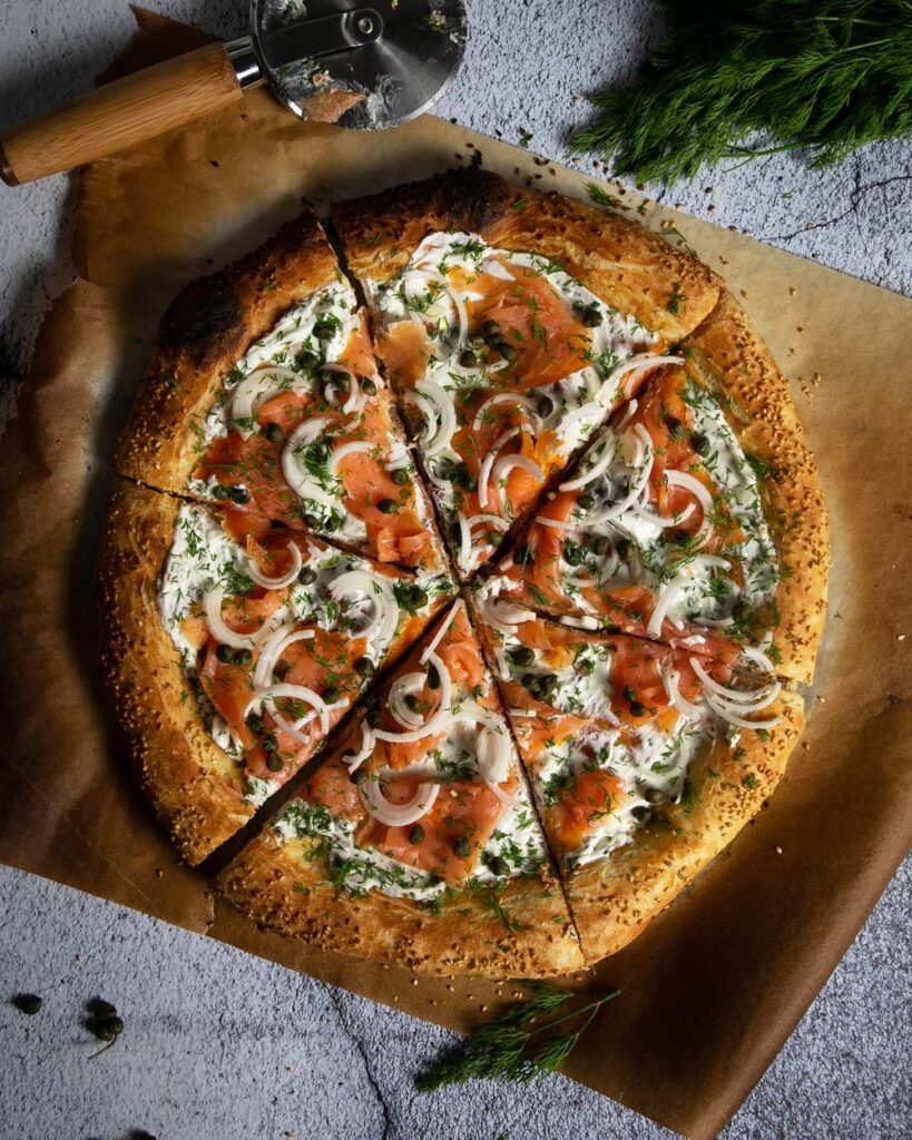 Top view of deli style breakfast pizza, sliced on parchment paper with a gray background