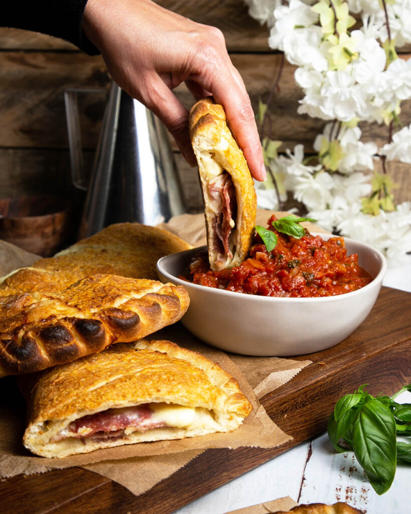 dipping a calzone in marinara sauce on a dark cutting board