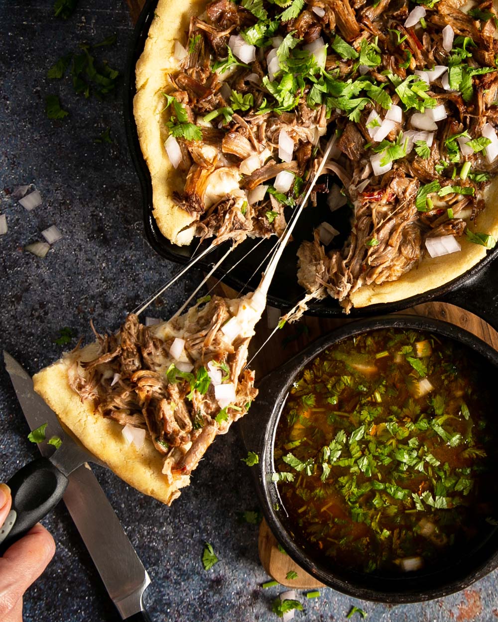 taking a slice of birria pizza in a cast iron with a side of consume