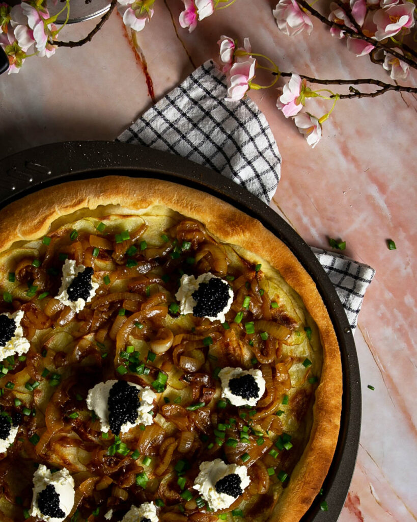 Top view of black caviar pizza in a pizza pan on a pink marble background