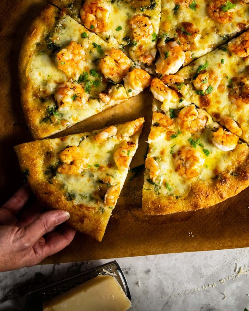 taking a slice of garlic parmesan shrimp pizza from a parchment paper
