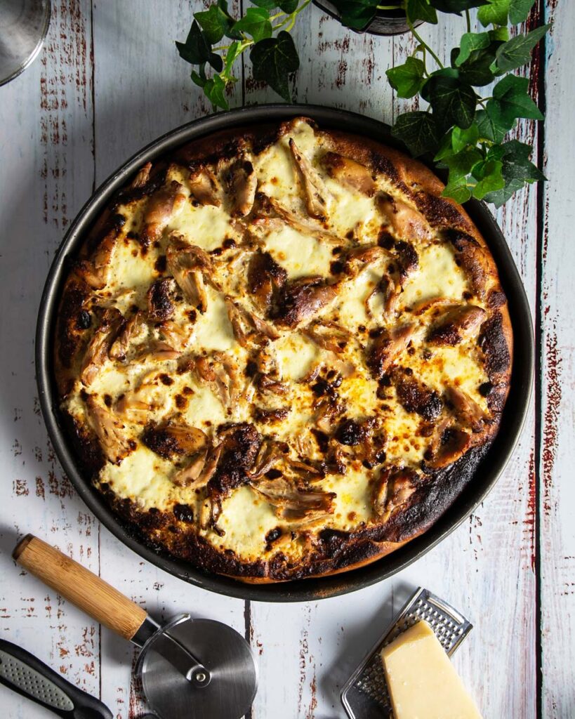 Top view of Jamaican jerk chicken pizza in a pan on a white wood background