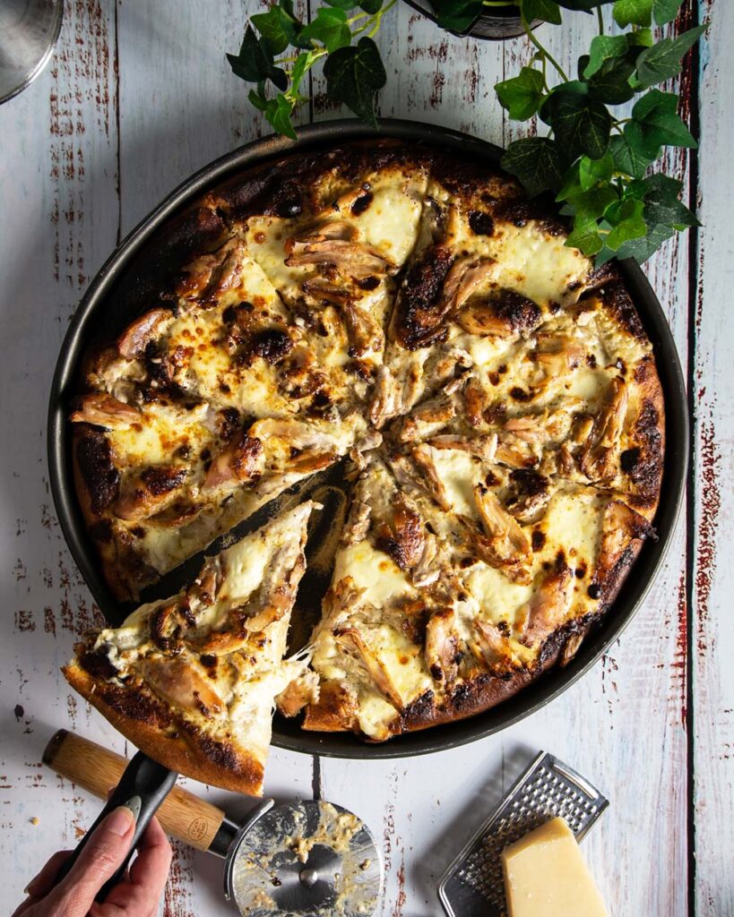 Taking a slice of Jamaican jerk chicken pizza on a whitewashed counter top