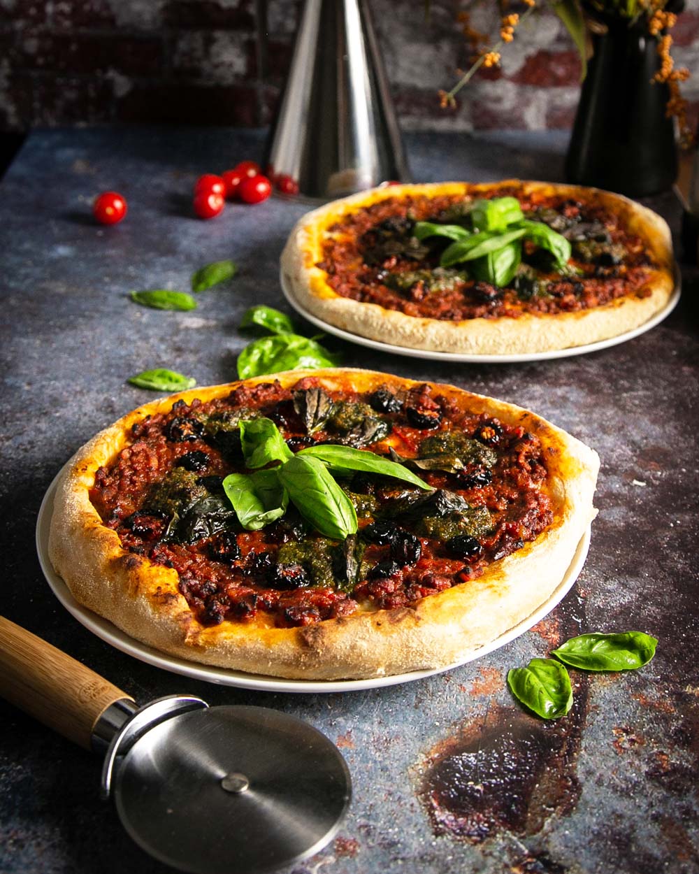 Angle view of 2 pesto Genovese pizza’s on plates with a dark marble background