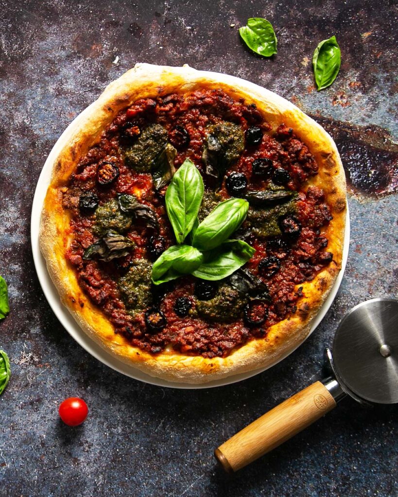 Top view of pesto Genovese pizza sprinkled with fresh basil on a dark background